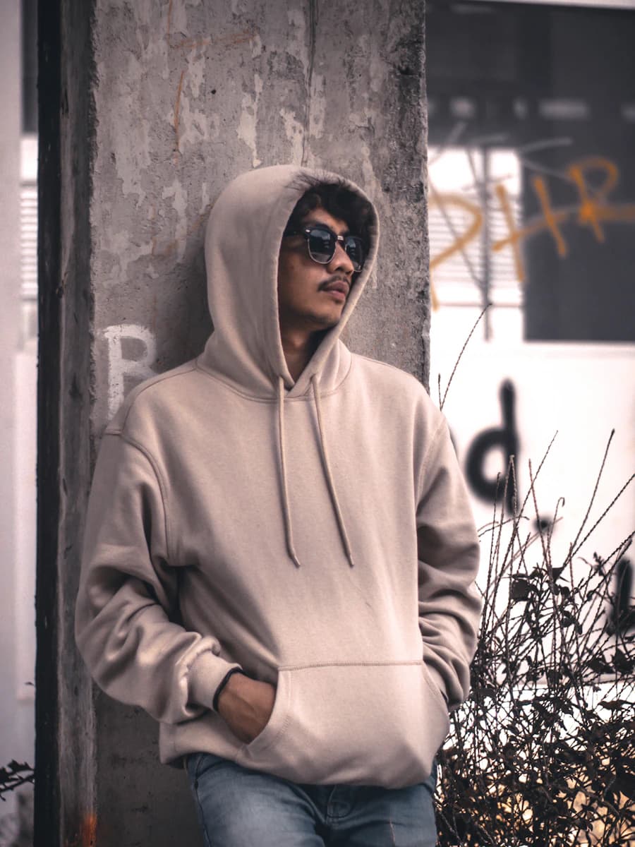 Adult model style reference — men wearing a grey hoodie jacket leaning in a wall during daytime